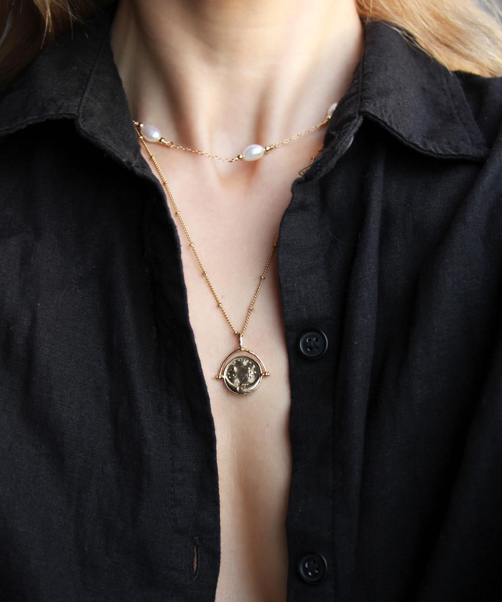 Gold Manifesting As Above So Below Spinner Necklace worn by woman with pearl necklace.