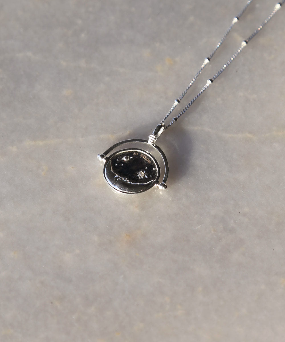 Sterling Silver Manifesting As Above So Below Spinner Necklace resting on marble.