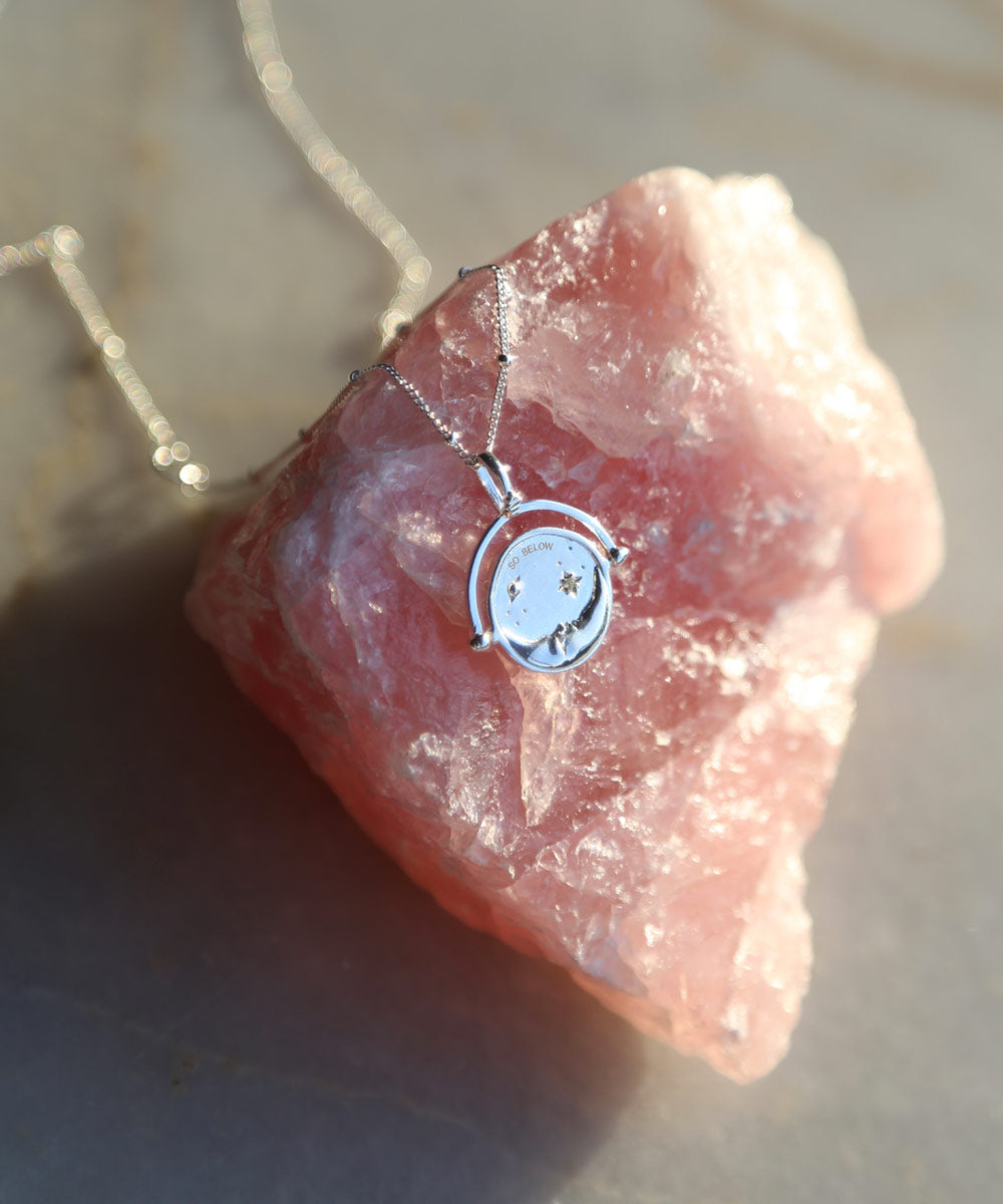 Sterling Silver Manifesting As Above So Below Spinner Necklace resting on rose quartz crystal stone.