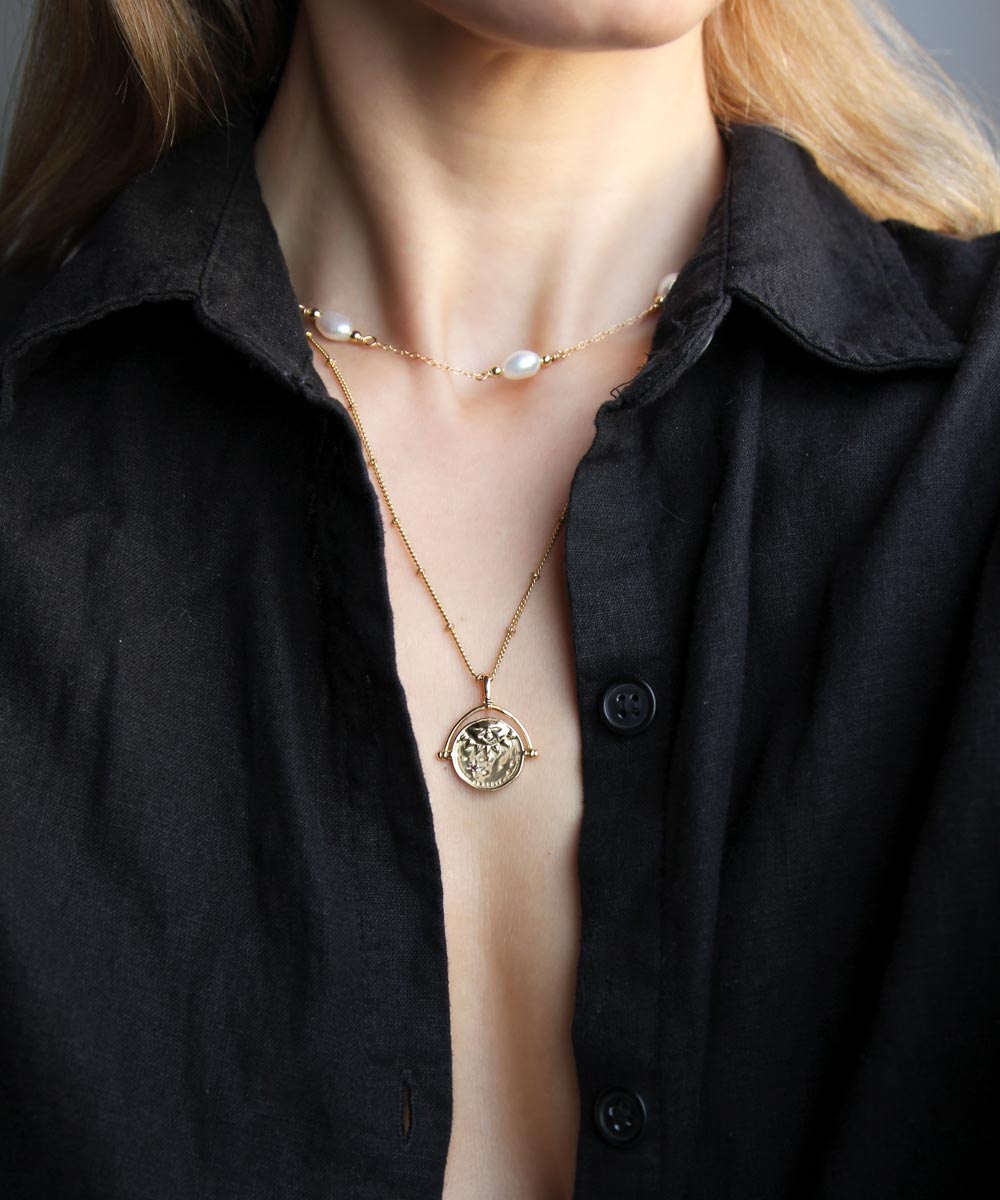 Gold Manifesting As Above So Below Spinner Necklace worn by woman with pearl necklace.