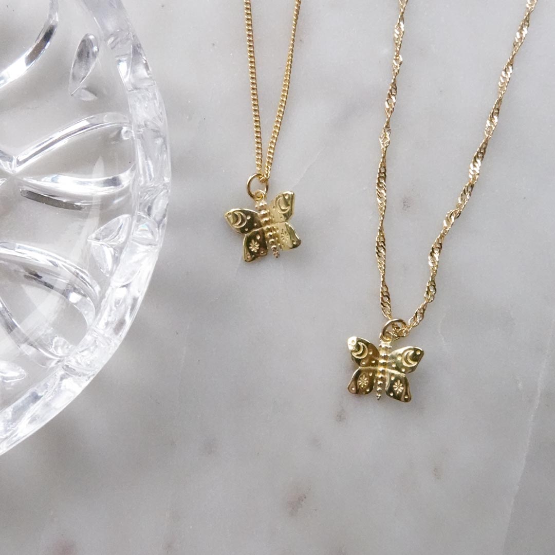 Australian gold filled butterfly charms with cosmic etchings on Singapore and curb chain necklaces and a marble background.