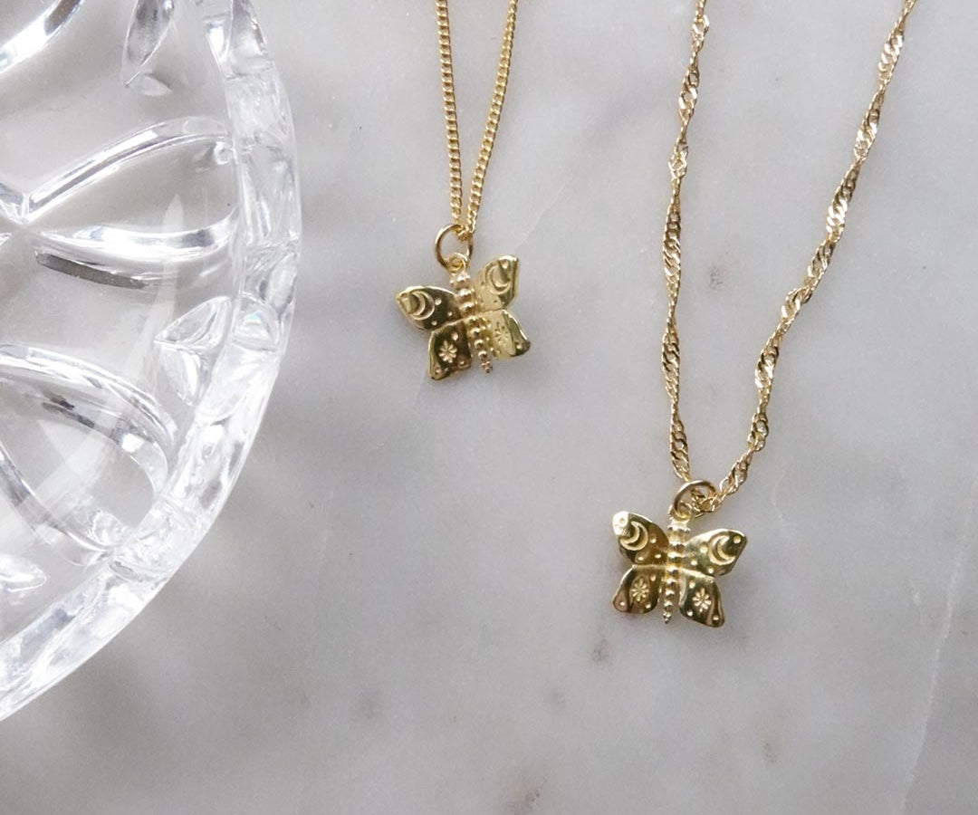 Australian gold filled butterfly charms with cosmic etchings on Singapore and curb chain necklaces and a marble background.