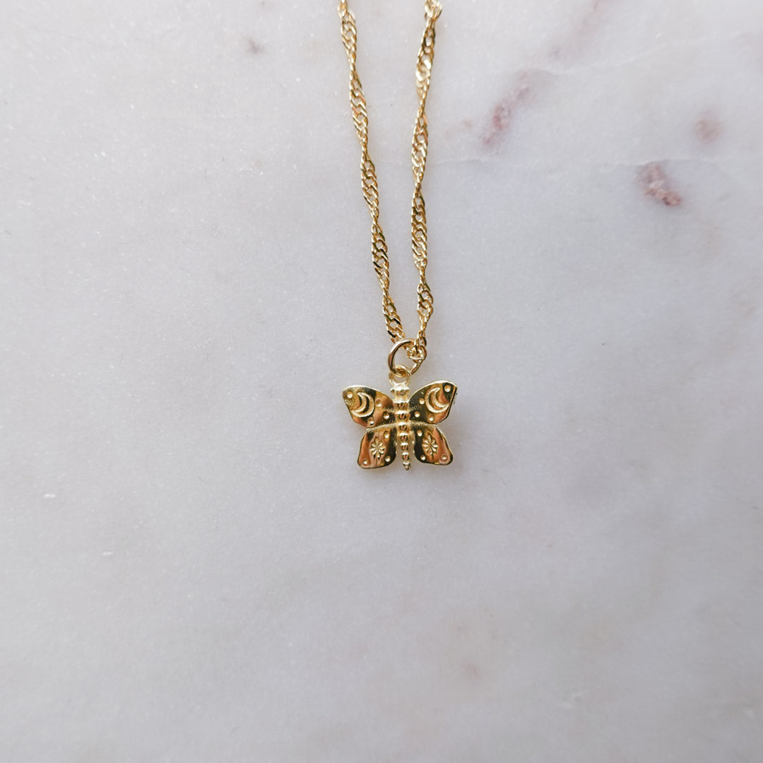 Australian gold filled butterfly charms with cosmic etchings on gold filled Singapore chain necklace and a marble background.
