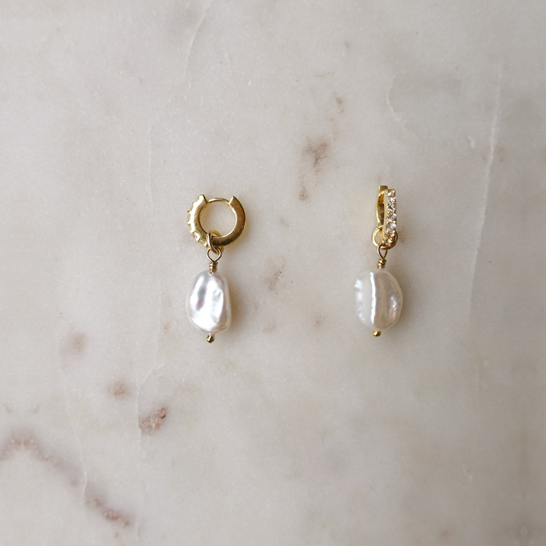 Australian gold filled huggies with white topaz stones and a freshwater pearl sit against a marble background.