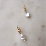 Gold filled huggies with white topaz stones and a freshwater pearl sit against a marble background.