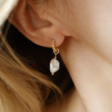 Woman wears gold filled huggies with white topaz stones and a freshwater pearl charm. Maribel earrings.