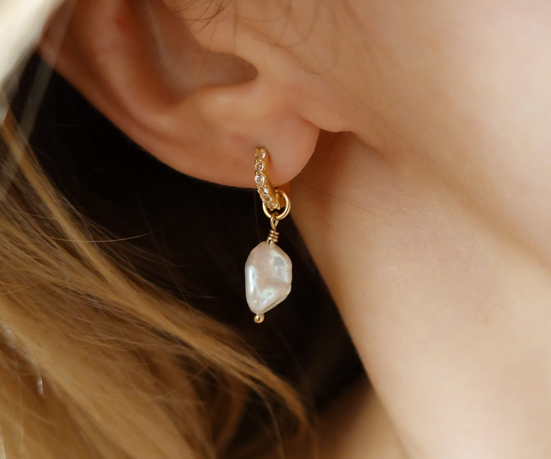 Woman wears gold filled huggies with white topaz stones and a freshwater pearl charm. Maribel earrings.