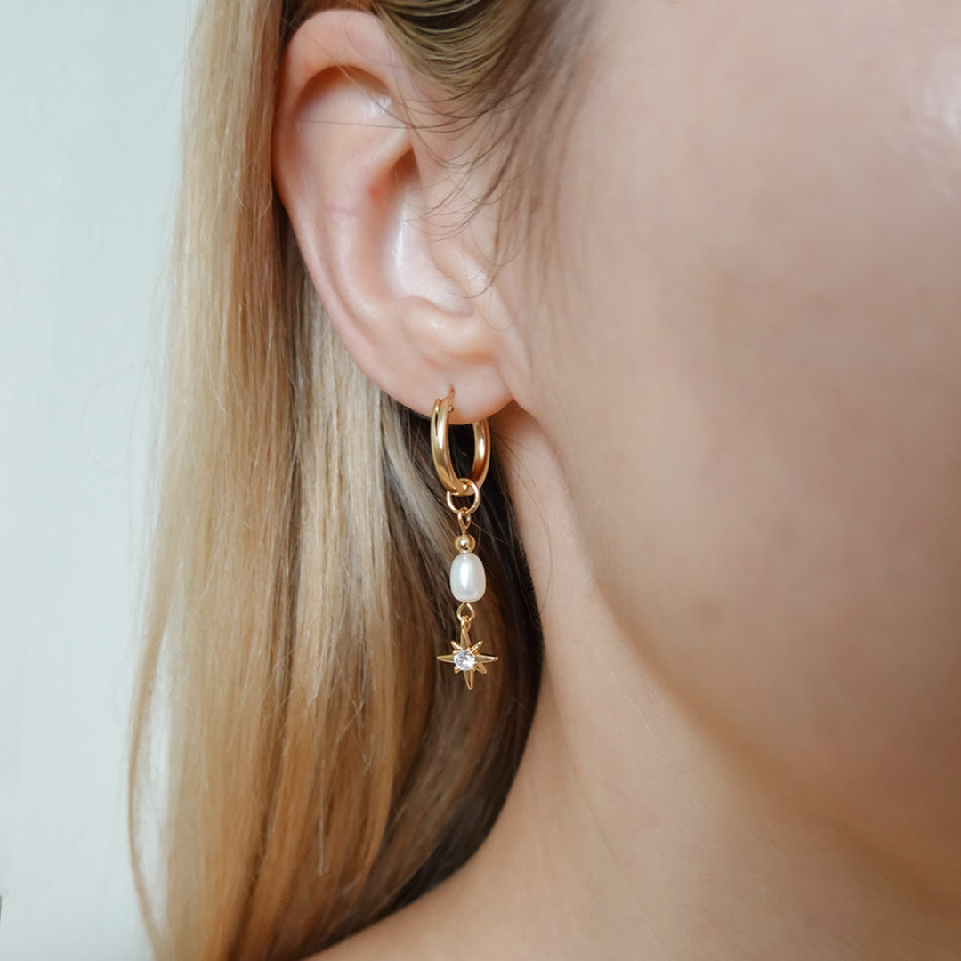 Woman wears a gold filled hoop earring with a freshwater pearl and north star charm.